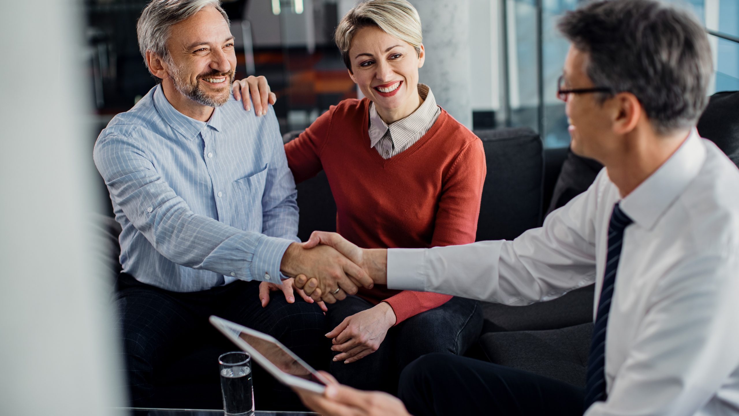 Happy couple handshaking with financial advisor after successful meeting in the office.